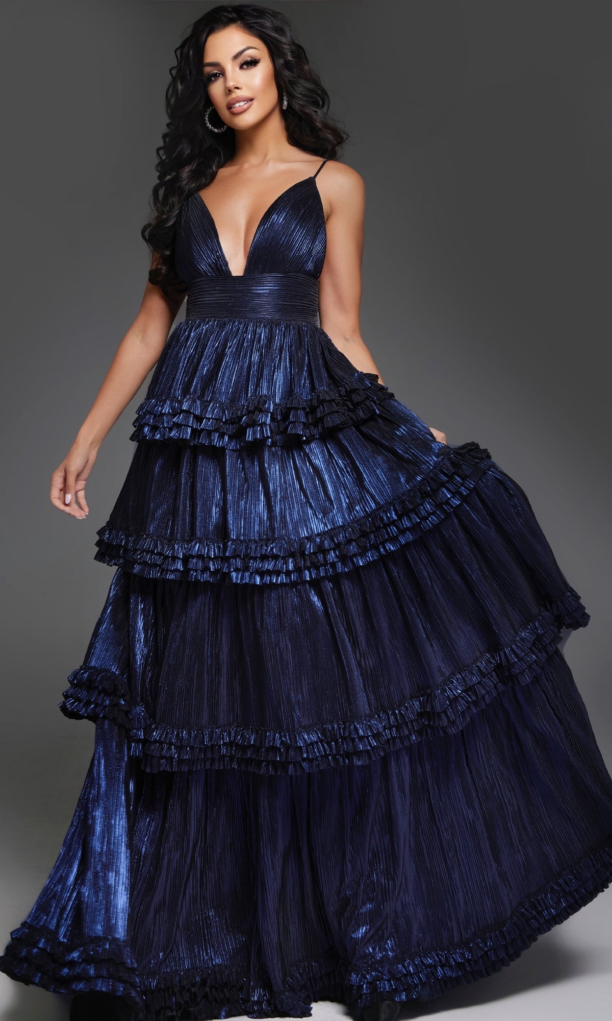 A woman poses elegantly in the Jovani 38296 Long Navy Prom Dress, featuring a sleeveless deep v-neck, tiered ruffles, and a full skirt against a dark background.